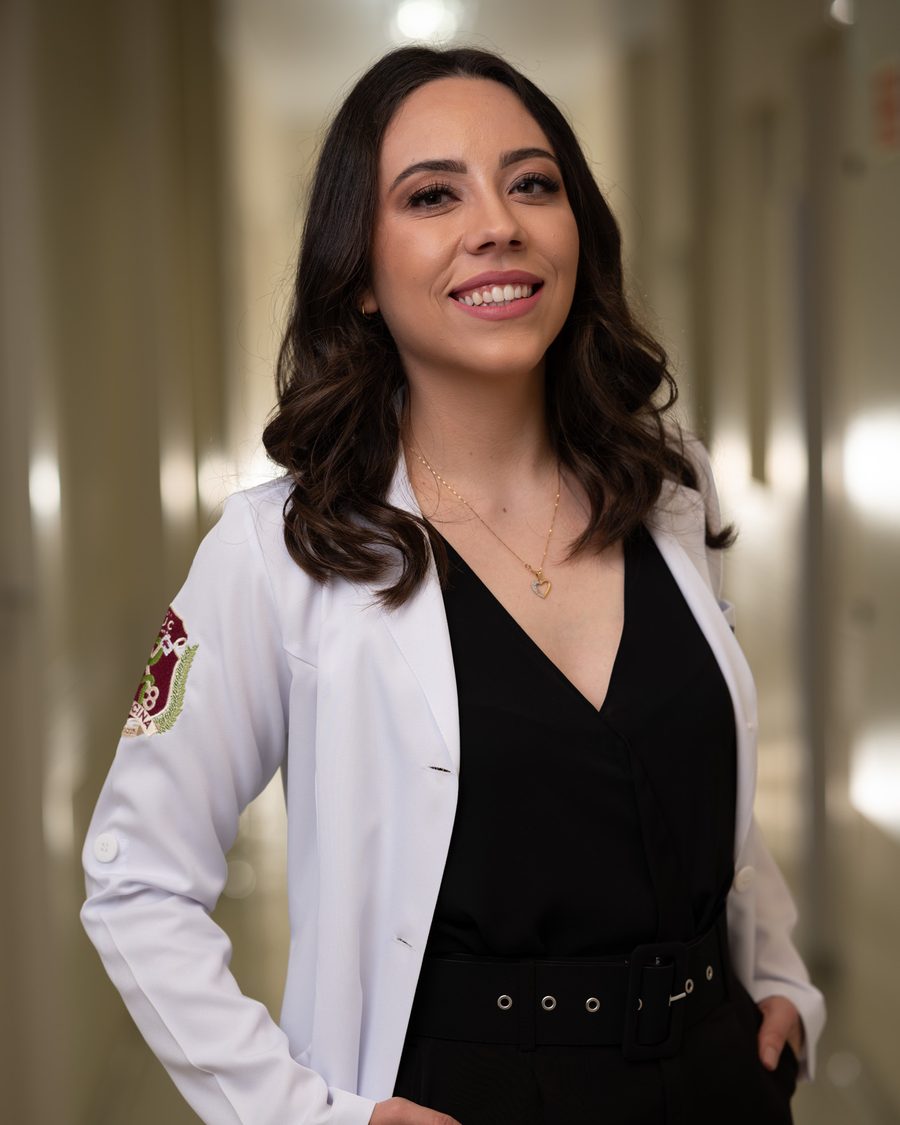 Dra. Isabelle Faoro de jaleco, em pé, sorrindo